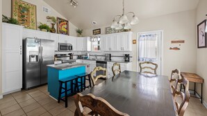 Una cocina con armarios blancos, una isla azul, electrodomésticos de acero inoxidable y sillas de madera alrededor de una mesa de madera oscura.