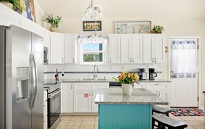 A kitchen with white cabinets, a stainless steel refrigerator, a coffee maker, and a window with a view.