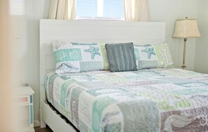 Ein Bett mit einer gesteppten Decke mit Meeresmotiven, einer Nachttischlampe und einem Fenster mit Vorhängen.