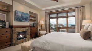 A bedroom with a fireplace, a large bed, a view of the city, and a painting on the wall.
