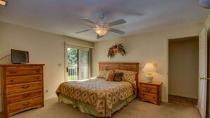 A bedroom with a bed, a dresser, a nightstand, a ceiling fan, and a door.