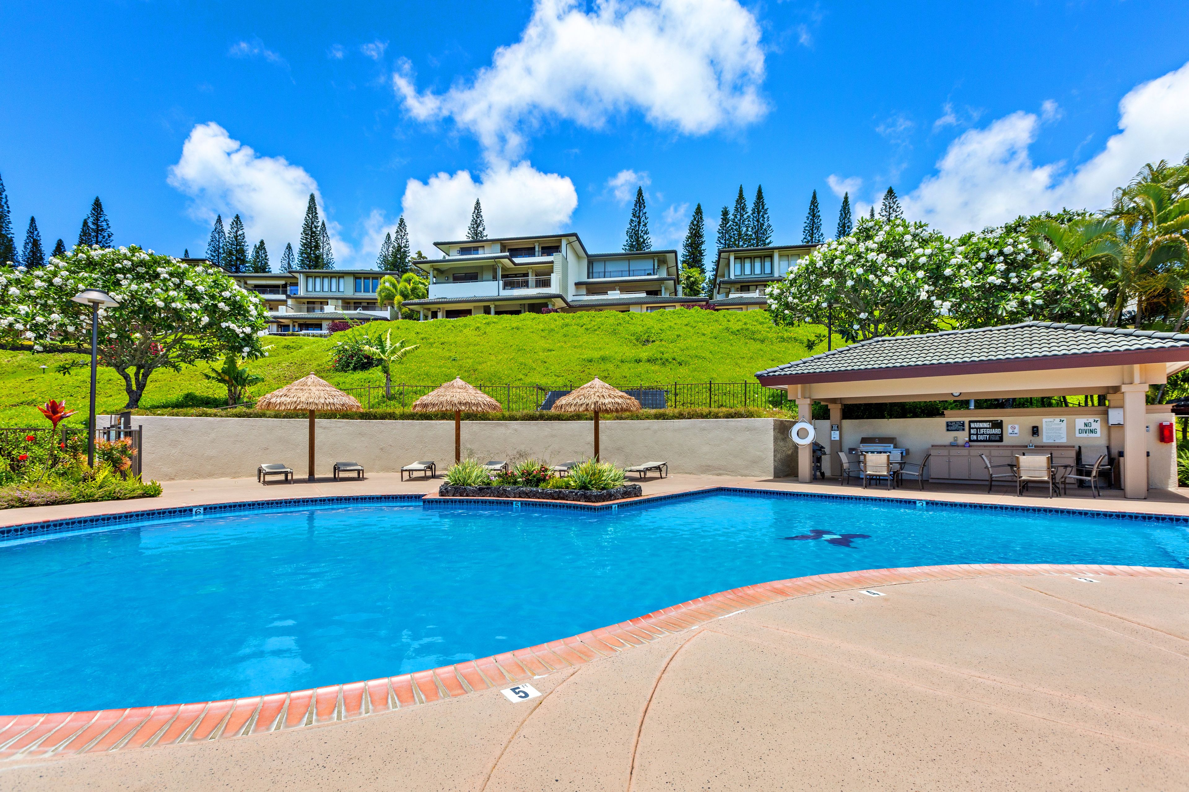 Una piscina con un patio circostante, una zona relax coperta e vista su edifici residenziali sullo sfondo.