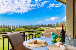 A table set with a bottle of Cline wine, two glasses, a napkin, a woven coo-coo bird ornament, and a yellow flower on a balcony overlooking a golf course and mountains.