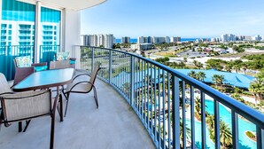 A balcony with a table and chairs, overlooking a cityscape and a pool area.