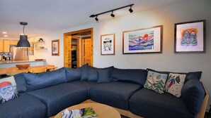 Un soggiorno moderno con un divano componibile, un'area pranzo con tavolo in legno e una cucina sullo sfondo.