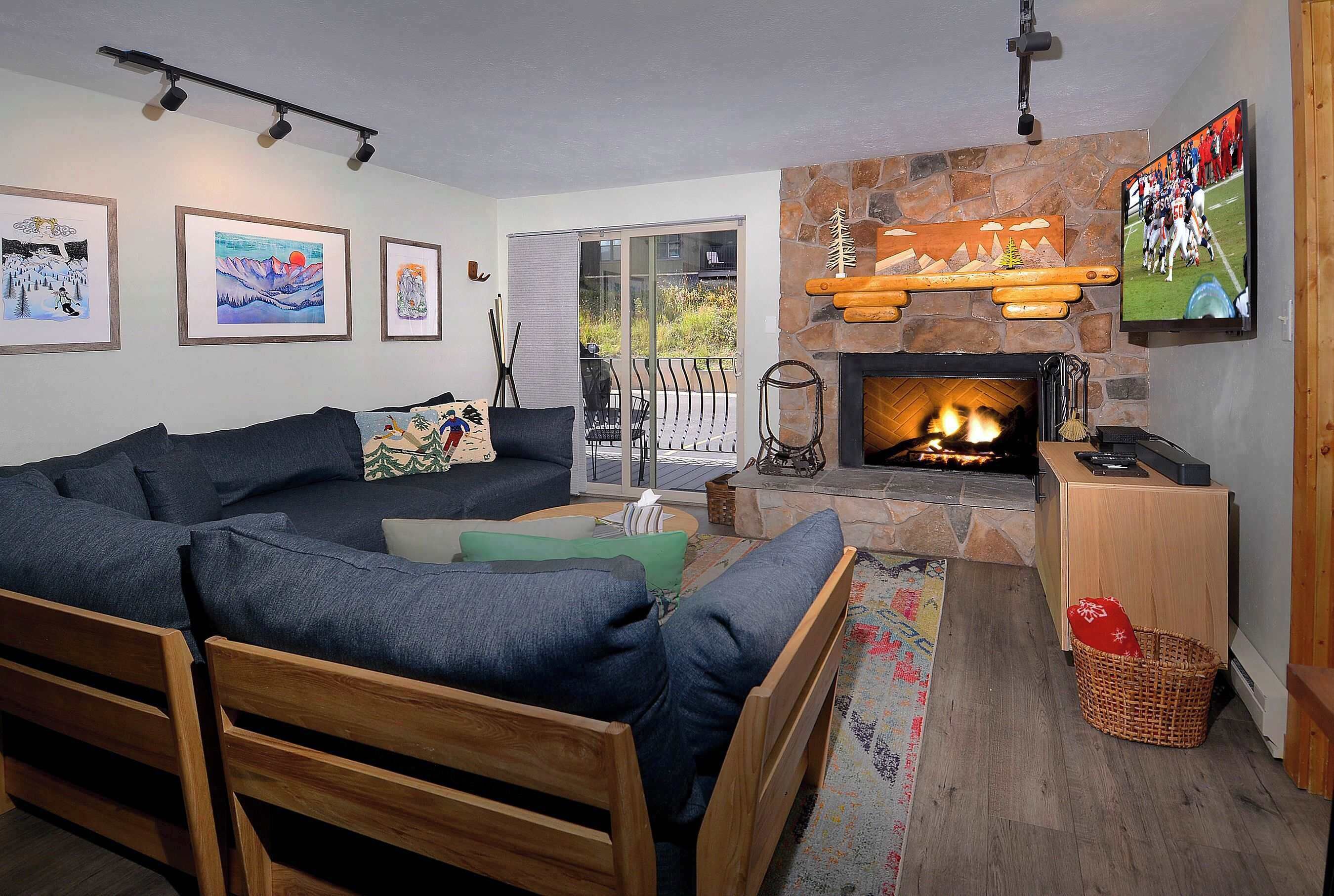 A cozy living room with a fireplace, a large sofa, and a television mounted on the wall.
