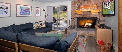 A cozy living room with a fireplace, a large sofa, and a television mounted on the wall.