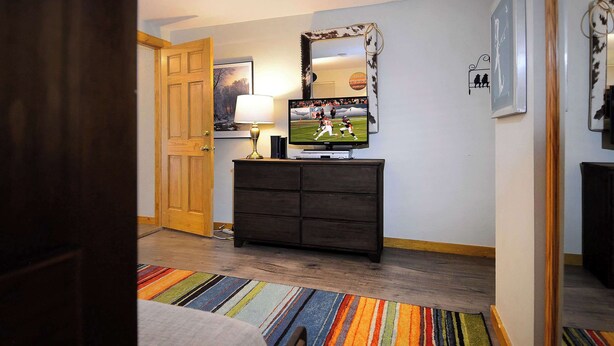 Un corridoio con una porta in legno, una televisione su un mobile, un tappeto decorato e uno specchio appeso al muro.