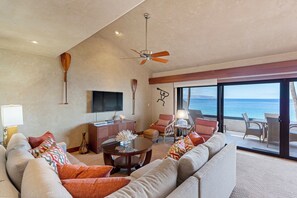 A spacious living room with a large sofa, a coffee table, and a ceiling fan. There is a TV mounted on the wall and a view of the ocean through large windows. - Experience beachfront luxury at Makena Surf #B-304, a stunning 2-bedroom retreat in Maui. (Makena, Maui)