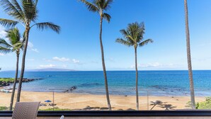 A beach view from a balcony with palm trees, a sandy beach, and the ocean. - Experience beachfront luxury at Makena Surf #B-304, a stunning 2-bedroom retreat in Maui. (Makena, Maui)
