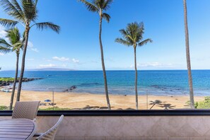 A beach view from a balcony with palm trees, a sandy beach, and the ocean. - Experience beachfront luxury at Makena Surf #B-304, a stunning 2-bedroom retreat in Maui. (Makena, Maui)