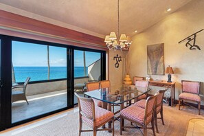 Un espace repas avec une table et des chaises en verre, un lustre et une vue sur l’océan.