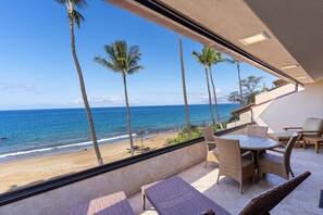Un balcon doté de meubles en osier, offrant une vue sur une plage et l’océan.