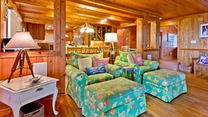 A cozy wooden cabin interior with a wooden ceiling, a dining area with a chandelier, and a seating area with patterned cushions. - Van Horne Villa | Beautiful Home, Ocean Views! (Tybee Island)