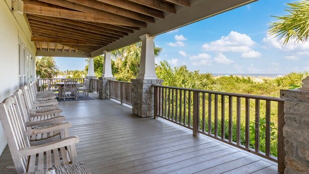 A covered outdoor area with wooden benches and a stone pillar, overlooking a beach with palm trees and a clear sky. - Van Horne Villa | Beautiful Home, Ocean Views! (Tybee Island)