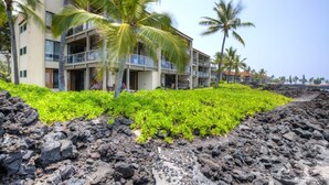 A hotel with a modern design, featuring a multi-story structure with balconies. The building is surrounded by lush greenery and palm trees. - Aloha Condos, Keauhou Kona Surf and Racquet Club, Condo 1-102, Oceanfront (Kailua Kona)