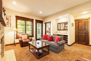 Una sala de estar con chimenea, sillón de cuero y sofá con cojines rojos.