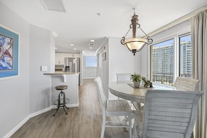 A modern kitchen with white cabinets, a stainless steel refrigerator, and a dining area with a round table and white chairs.