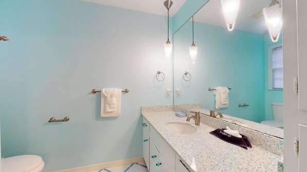 A bathroom with a light blue wall, a white toilet, a sink with a mirror, and two towel rings.