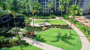 A hotel courtyard with palm trees, a small pond, and a pool area.