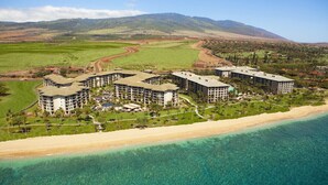 A coastal hotel with multiple buildings, a beachfront, and a mountainous backdrop.