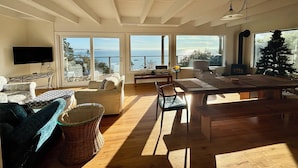 Un salon spacieux doté d’une grande fenêtre donnant sur la mer, d’une cheminée et d’un téléviseur fixé au mur.