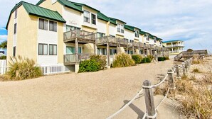 A row of beachside motel buildings with balconies, a sandy path, and a wooden fence. - Tybee Lights 112B | Pet Friendly, Incredible Views (Tybee Island)