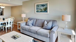A living room with a grey sofa, white chairs, a white coffee table, and a painting on the wall. - Tybee Lights 112B | Pet Friendly, Incredible Views (Tybee Island)