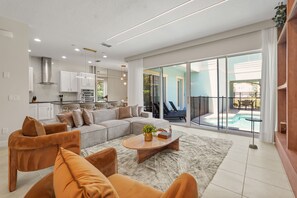 Ein modernes Wohnzimmer mit einer Couch, Sesseln, einem Couchtisch und Blick auf einen Pool durch große Glasfenster.