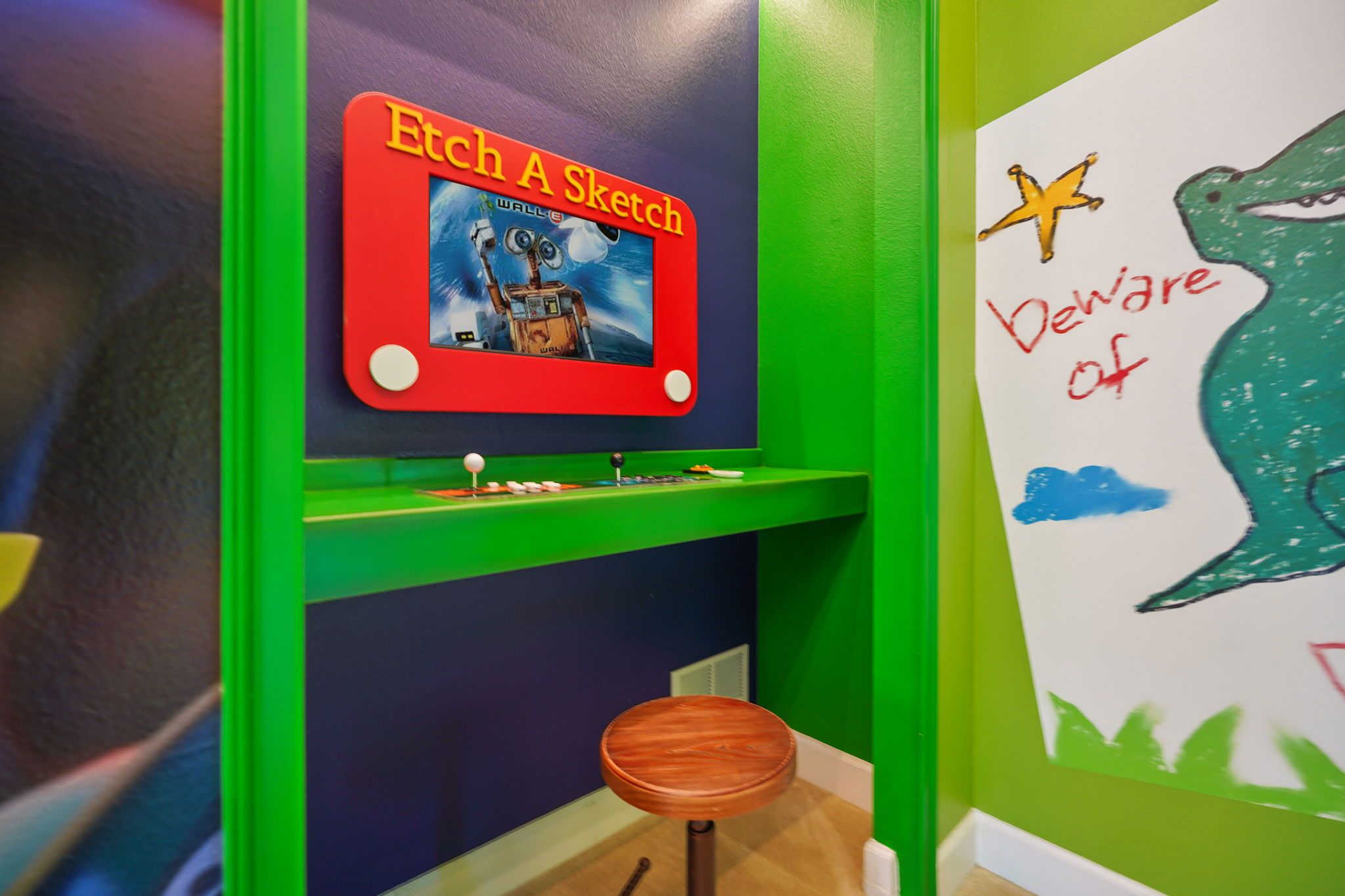 A children's play area with a red and green wall, a small stool, and a wall with a drawing and text.
