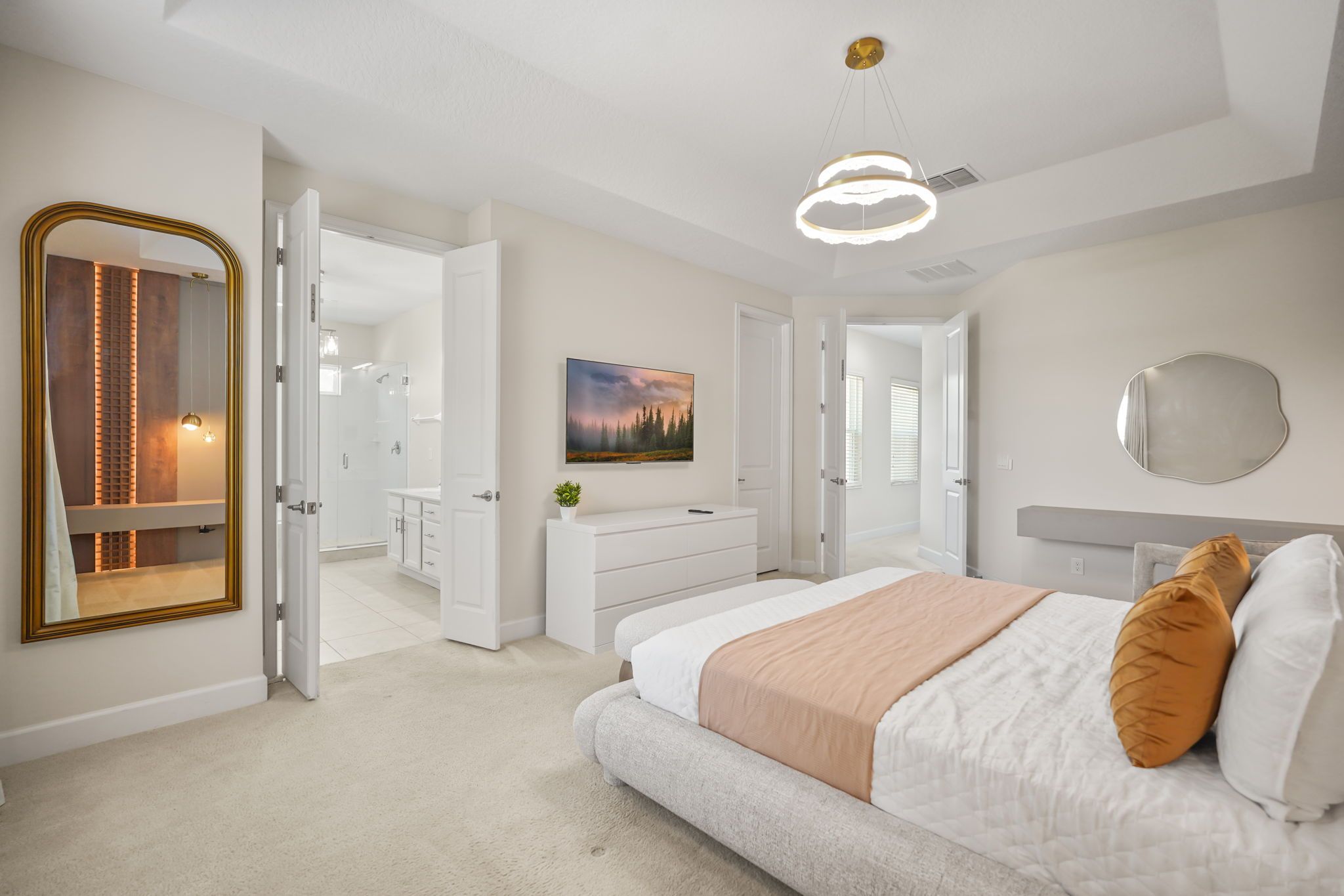 A modern bedroom with a large bed, a vanity, and a walk-in closet.