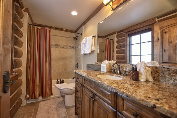 A bathroom with a stone shower, a double sink vanity, and wooden cabinetry.