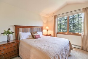 Un dormitorio con una cama grande, una mesita de noche con lámpara, un aparador y una ventana con cortinas.