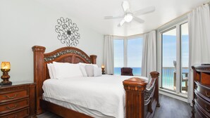 Une chambre spacieuse avec un grand lit, une tête de lit en bois et une vue sur l’océan grâce à de grandes fenêtres.