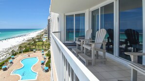 Un balcon agrémenté de chaises Adirondack blanches, une piscine et une vue sur la plage et l’océan.