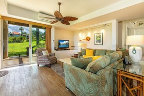 A spacious living area with a large sofa, a television, and a ceiling fan.