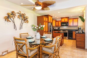 A modern kitchen with wooden cabinets, a stainless steel refrigerator, and a dining area with wicker chairs and a glass table.