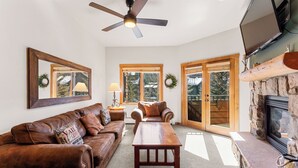 A living room with a brown leather sofa, a wooden coffee table, a fireplace, and a ceiling fan. - Short Walk to Lifts, Shops, and Dining! Private Balcony with Slope Views (Keystone)