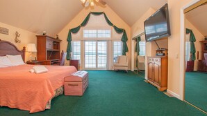 Ein Schlafzimmer mit einem großen Bett, einem Schminktisch, einem Fernseher und Blick ins Freie durch ein Fenster.