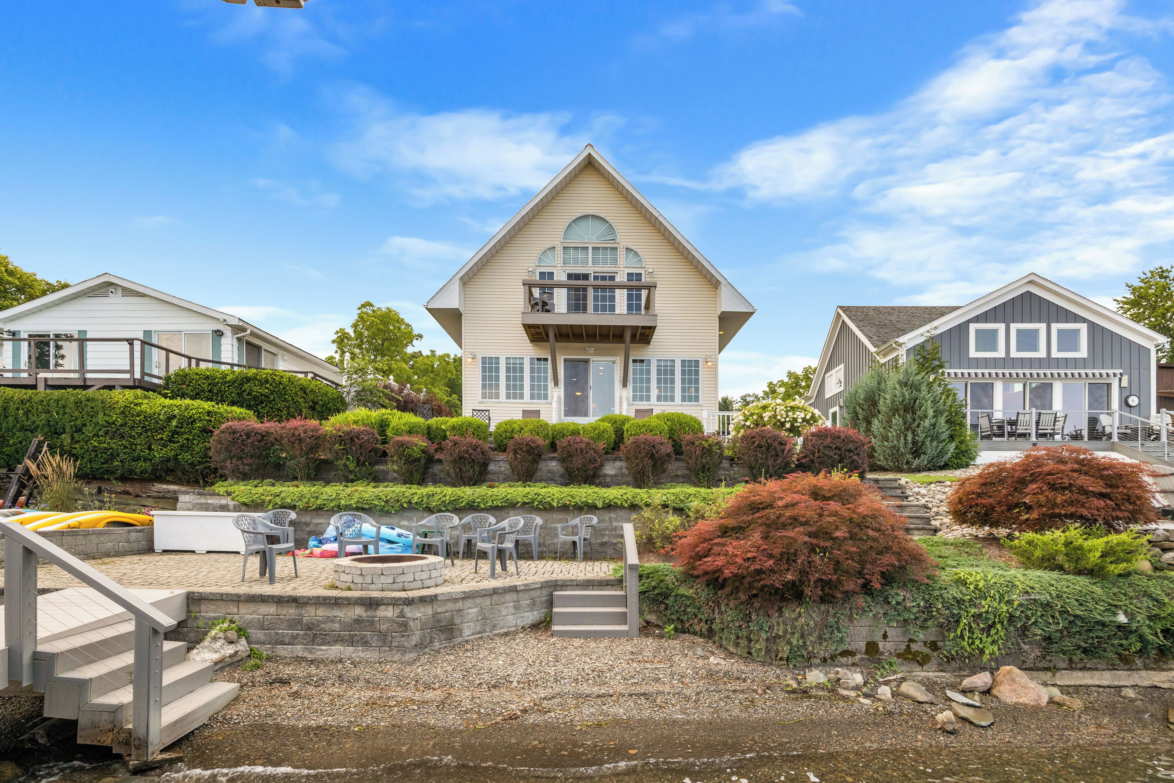A two-story house with a balcony and a small deck area with chairs and a pool.