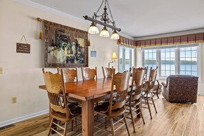 A dining area with a wooden table and chairs, a chandelier, a painting, and a view of the outdoors.