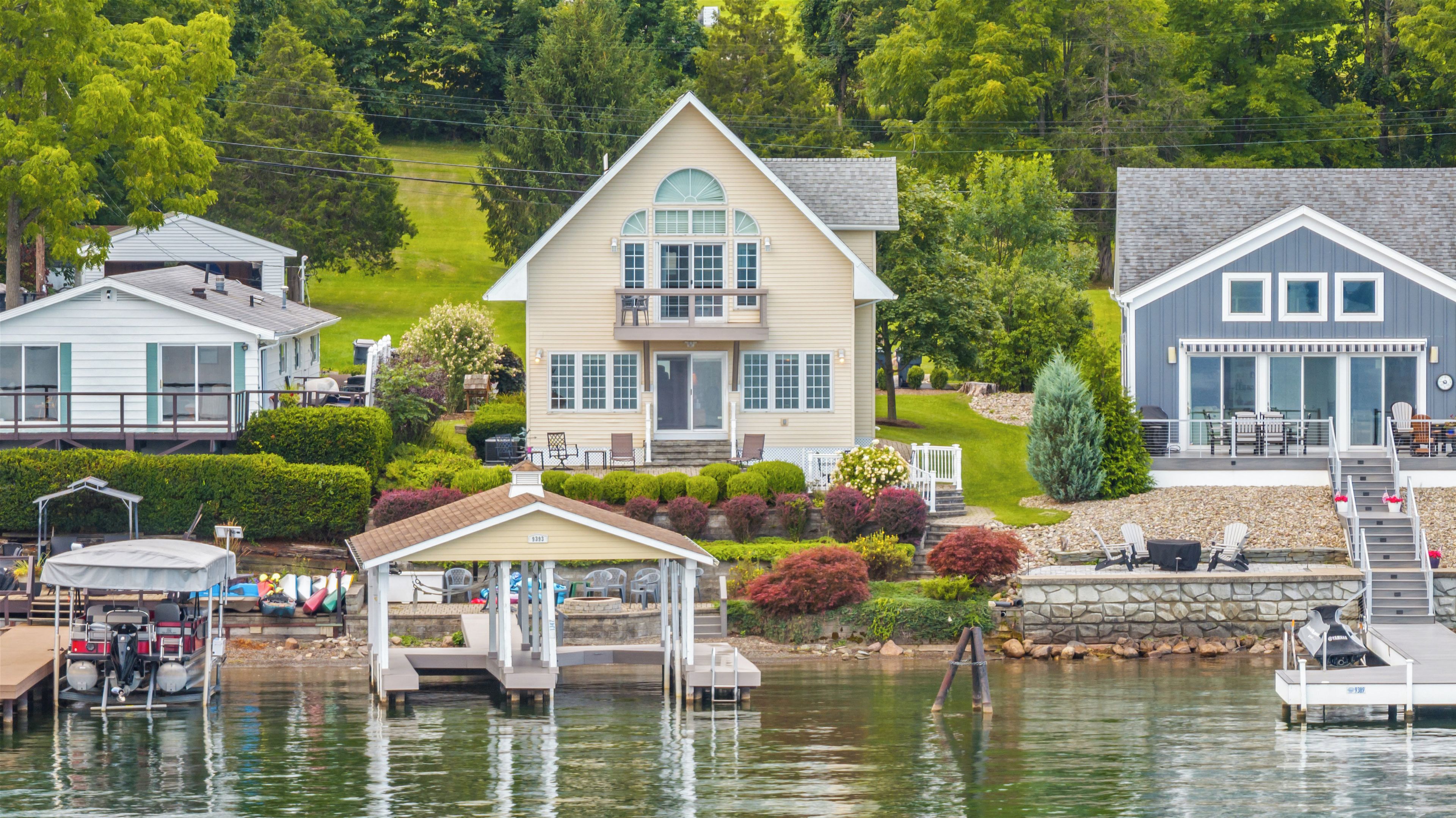 A waterfront property with a main house featuring a balcony, a covered dock area, and a stone wall.