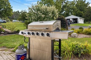 Un barbecue au gaz portatif, doté d’une cheminée, d’une bouteille de propane et avec un garage en arrière-plan.