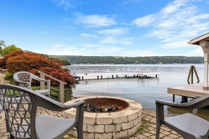 Une terrasse au bord du lac, avec un foyer, des chaises et une vue sur l’eau.