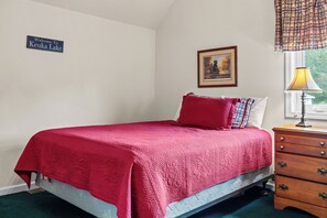 Une chambre à coucher avec un lit, une table de chevet, une lampe, un tableau encadré et une pancarte de bienvenue.