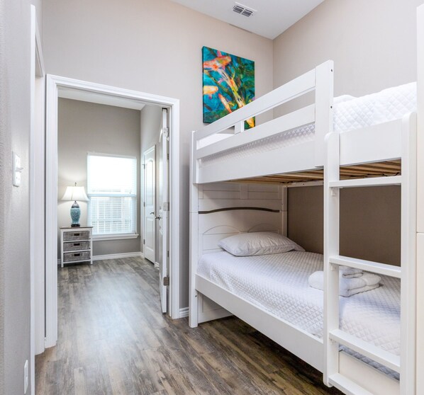 Um quarto com beliches, uma janela com persianas, um abajur e um quadro na parede.