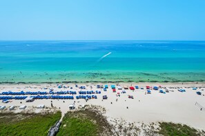 A beach with rows of umbrellas and beach chairs, a clear blue sea, and a sandy shore.