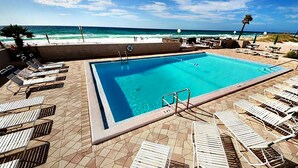Una piscina rectangular con agua azul cristalina, rodeada de sillas de descanso y una terraza con baldosas.