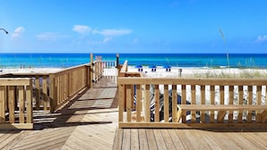 Un muelle de madera que conduce a una playa con aguas azules cristalinas y algunas personas a lo lejos.