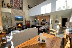 Un amplio salón con chimenea, televisor y comedor con una mesa dispuesta para dos.